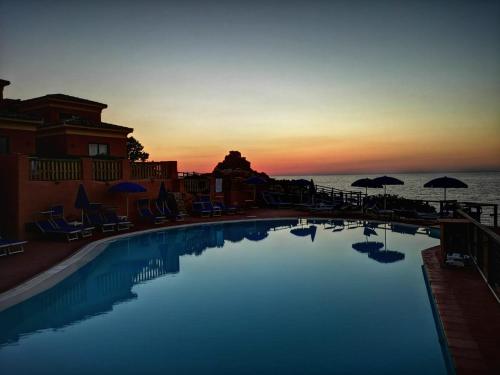 ein Pool mit Stühlen und Sonnenschirmen bei Sonnenuntergang in der Unterkunft Hotel Costa Paradiso in Costa Paradiso