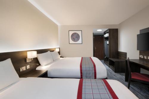 a hotel room with two beds and a desk at Ramada by Wyndham Leeds East in Leeds