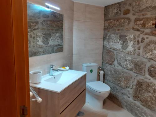 a bathroom with a sink and a toilet and a stone wall at A casa do pátio in Montalegre