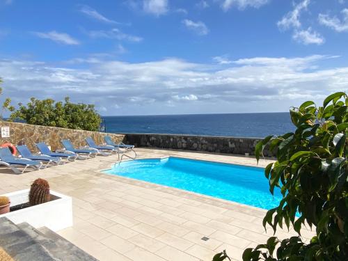 a swimming pool with chairs and the ocean in the background at Seafront Puerto Calero Villa in Puerto Calero