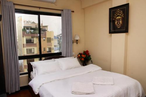 1 dormitorio con 1 cama con sábanas blancas y ventana en Hotel Buddha Land, en Katmandú