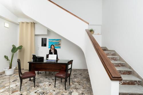 a woman sitting at a desk under a stairs with a laptop at Regina Margherita - Bed and Breakfast & Rooftop Lounge Bar in Siracusa