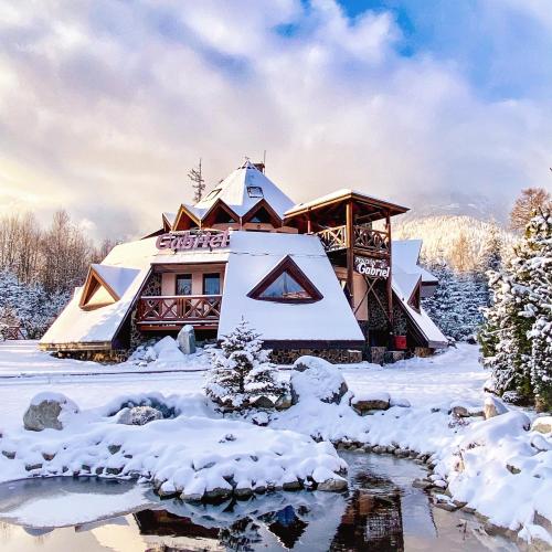 a building covered in snow next to a stream at Penzion Gabriel in Smokovce