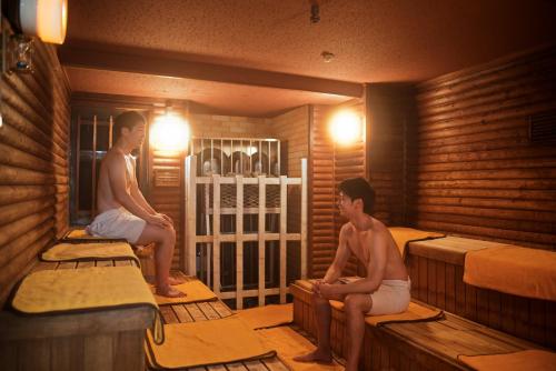 two men sitting on beds in a sauna at Shinjuku Kuyakusho-mae Capsule Hotel in Tokyo