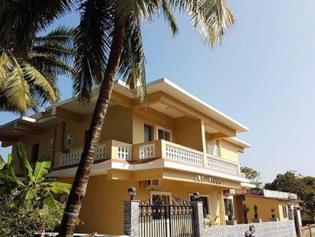 a yellow house with a balcony and two palm trees at JMD VILLA in Vagator