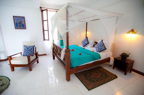a bedroom with a canopy bed and a chair at Flame Tree Cottages in Nungwi