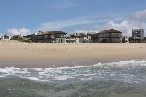 a beach with houses in the background and the ocean at MarAdentro Apart Hotel & Suites in Punta Del Diablo