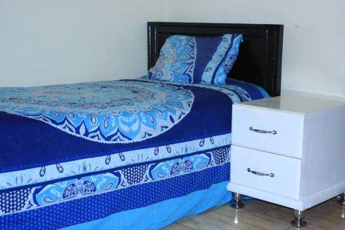 a bed with a blue comforter and a white dresser at DREAM APARTMENTS UGANDA in Kampala