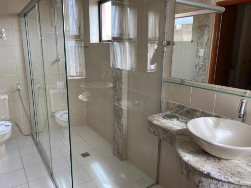 a bathroom with a sink and a glass shower at Hotel Plaza Inn Flat Residence in Alfenas