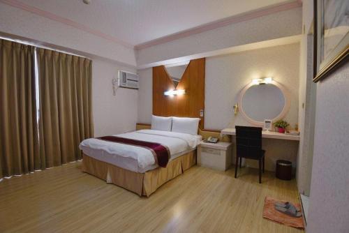 a hotel room with a bed and a desk and a mirror at Green Yard Business Hotel in Miaoli
