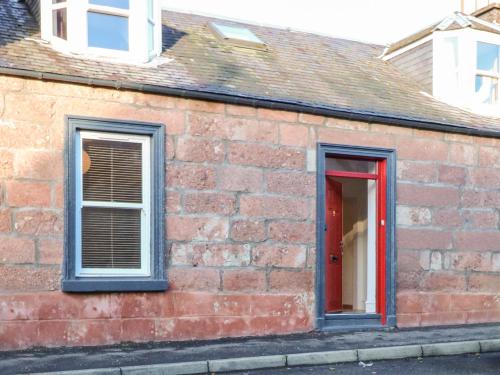 a brick building with two windows and a red door at George Cottage in Blairgowrie