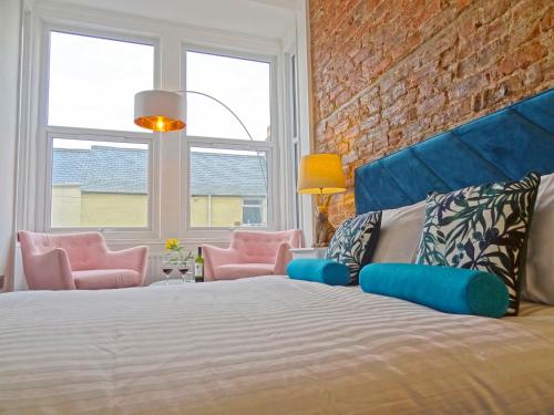 a bedroom with a bed and two pink chairs at Sea Coast Apartment by Seaside Llandudno in Llandudno