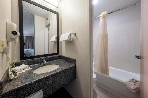 a bathroom with a sink and a mirror and a tub at HomeTown Inn by Red Roof East Syracuse in East Syracuse