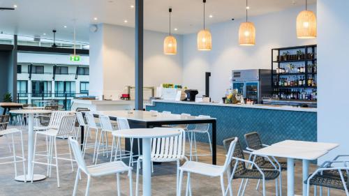 a restaurant with white chairs and tables and a bar at Oaks Cairns Hotel in Cairns