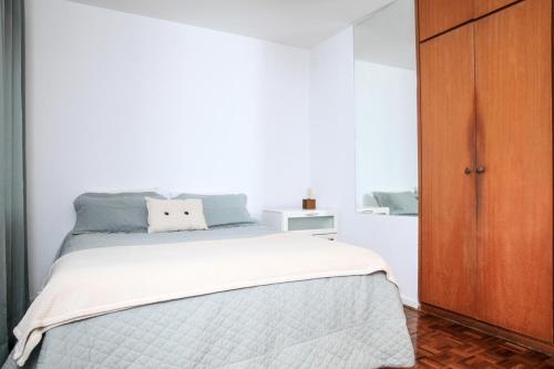 a white bedroom with a bed and a wooden cabinet at Vila Olimpia Jade in São Paulo