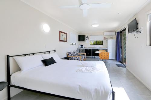 a bedroom with a white bed and a kitchen at Cane Village Holiday Park in Bundaberg