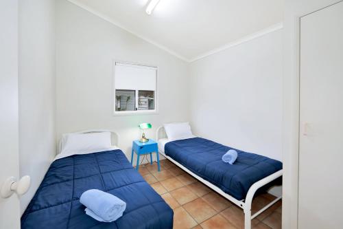 two beds in a white room with a blue blanket at Cane Village Holiday Park in Bundaberg