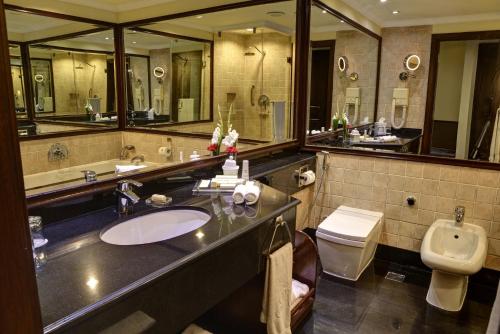 a bathroom with a toilet, sink, and mirror at Pearl Continental Hotel, Lahore in Lahore