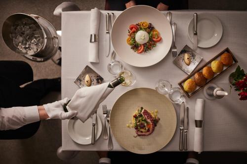a table with plates of food and a person holding a wine glass at Grand Hotel Vilnius, Curio Collection by Hilton in Vilnius