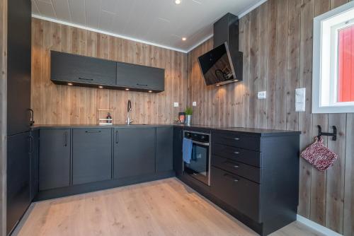 a kitchen with black cabinets and a tv on the wall at Seafront new cabin in Lofoten in Ballstad