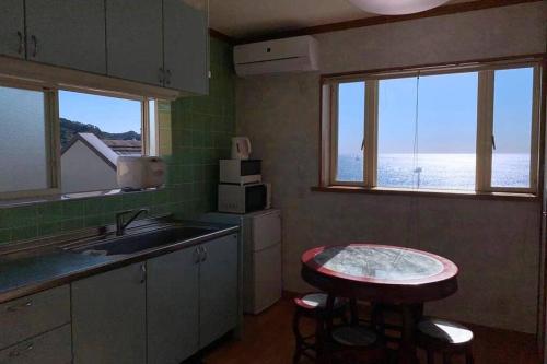 cocina con fregadero, mesa y 2 ventanas en Uhome Kamogawa Villa, en Kamogawa