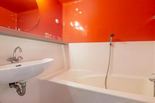 La salle de bains est pourvue de murs orange, d'un lavabo et d'une baignoire. dans l'établissement LES ARCS 1800 Village du Charvet, à Bourg-Saint-Maurice