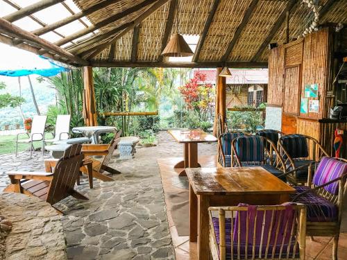 un patio al aire libre con mesas, sillas y una sombrilla en Pacific Edge Eco Lodge, en Dominical