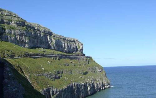 a rocky mountain with grass on it next to the ocean at Coastal Gem Apartment by Seaside Llandudno in Llandudno