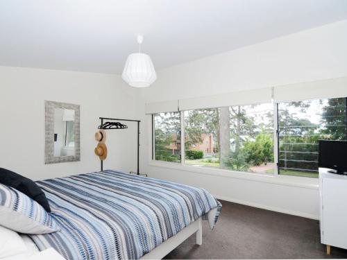 a white bedroom with a bed and a window at Acacia on Orion by Jervis Bay Rentals in Vincentia