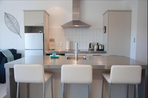 a kitchen with a counter with white chairs in it at The Condo On The Beach - Onetangi - Luxury at The Sands by Waiheke Unlimited in Onetangi