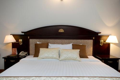 a bedroom with a large white bed with a wooden headboard at Hotel Sarina in Dhaka