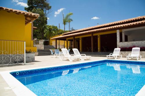 a swimming pool with white chairs and a house at Casarao Hostel - Analandia SP in Analândia