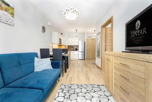Jantar Apartamenty - Apartamenty KASPROWICZA في كولوبرزيغ: غرفة معيشة مع أريكة زرقاء ومطبخ