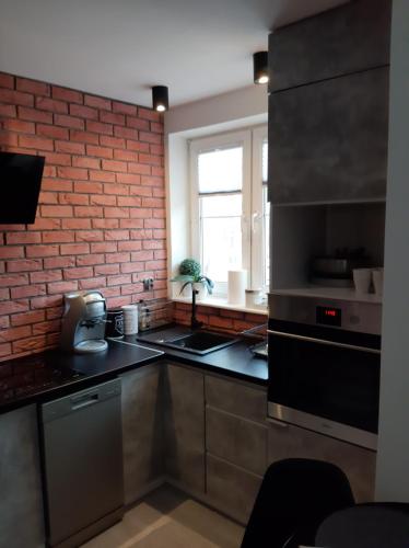 kuchnia ze sprzętem ze stali nierdzewnej i ceglaną ścianą w obiekcie Apartament Port w Ostródzie