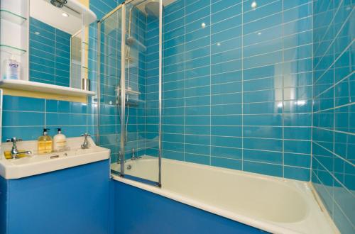 baño de azulejos azules con bañera y lavamanos en TDM Bachelot Lettings Ltd, en Londres