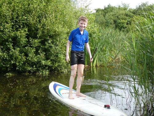 a young boy standing on a surfboard in the water at Devon Eco Lodges in Winkleigh