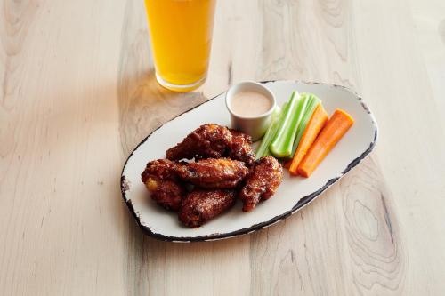 a plate of chicken wings and vegetables with a glass of orange juice at Holiday Inn - Erie by IHG in Erie
