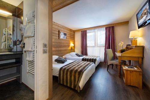 ラ・クリュサにあるHotel Alpen Rocのベッド2台とデスクが備わるホテルルームです。