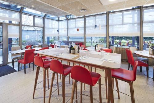 un restaurante con una mesa grande y sillas rojas en Campanile Argenteuil, en Argenteuil