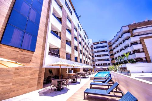 a pool with chairs and umbrellas next to a building at GOLDFLAT Cabo Branco by PenareiaTurBr in João Pessoa