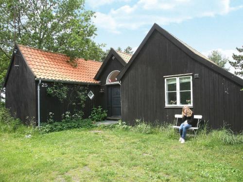 une femme assise sur un banc devant une maison noire dans l'établissement 10 person holiday home in Askeby, à Askeby