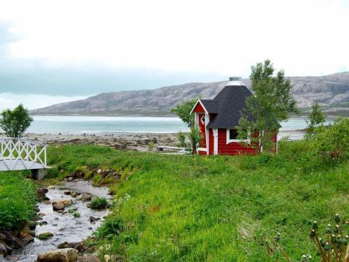 6 person holiday home in Vevelstad في Vevelstad: منزل احمر على تل بجوار نهر