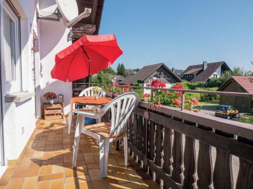 einen Tisch und Stühle auf einem Balkon mit einem roten Regenschirm in der Unterkunft Flat in Herrischried Black Forest in Herrischried