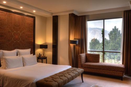 a bedroom with a bed and a chair and a window at Pearl Continental Hotel, Muzaffarabad in Muzaffarabad