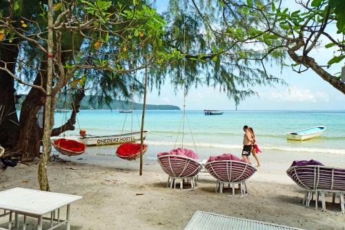 a woman walking on a beach with chairs and a swing at Onederz Koh Rong Sanloem in Koh Rong Sanloem