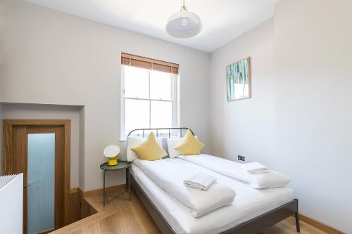 ein weißes Schlafzimmer mit einem Bett mit gelben Kissen in der Unterkunft Stylish Stays by Russel Square in London