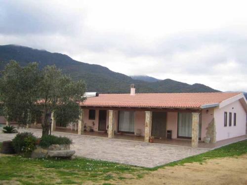 a house with a red roof with mountains in the background at Agriturismo Sa Mandria in Castiadas