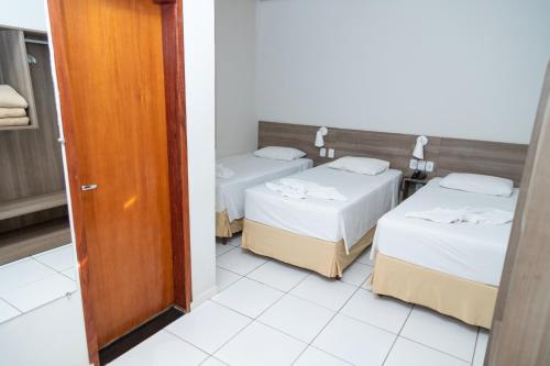 two beds in a small room with a door at Hotel BR 364 in Cacoal