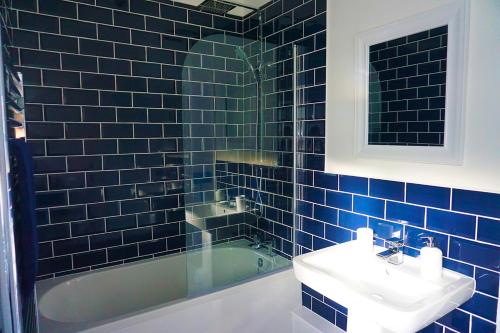baño de azulejos azules con lavabo y bañera en Staycation at Pine Cottage, a newly refurbished holiday cottage, en Goodwick