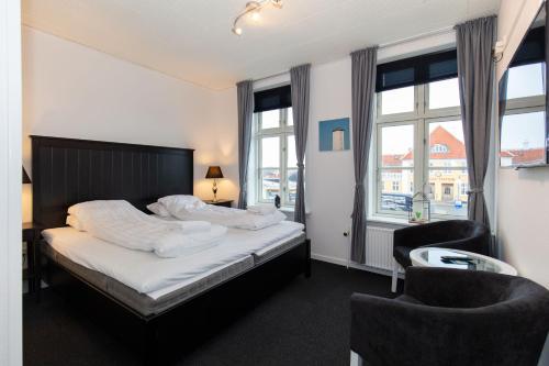 a bedroom with a bed and two chairs and windows at Skagen Hotel in Skagen